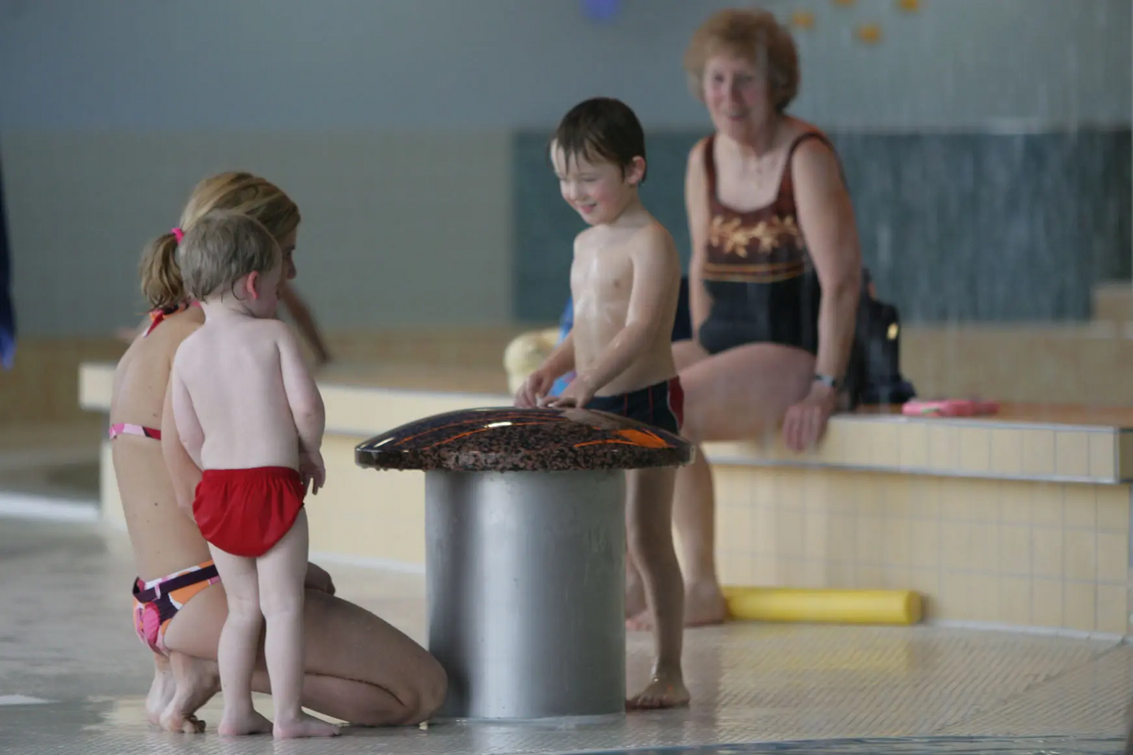 Junge Mutter mit zwei Kindern am Wasserpilz im Kinderbereich im LEUZE.