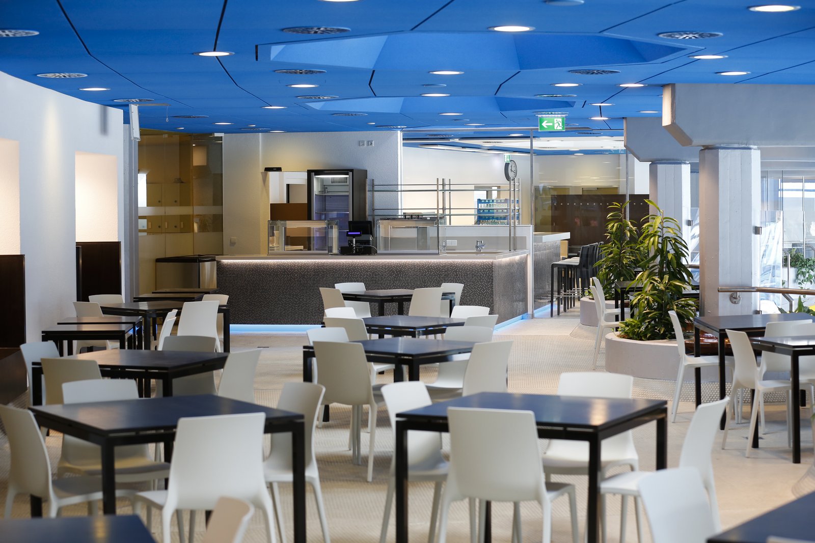 Das Bild zeigt das Restaurant in der Therme LEUZE: Ausgabetheke mit einer Bar-Theke, rechteckige Tische mit passenden Stühlen. Es sind keine Gäste auf dem Bild zu sehen.