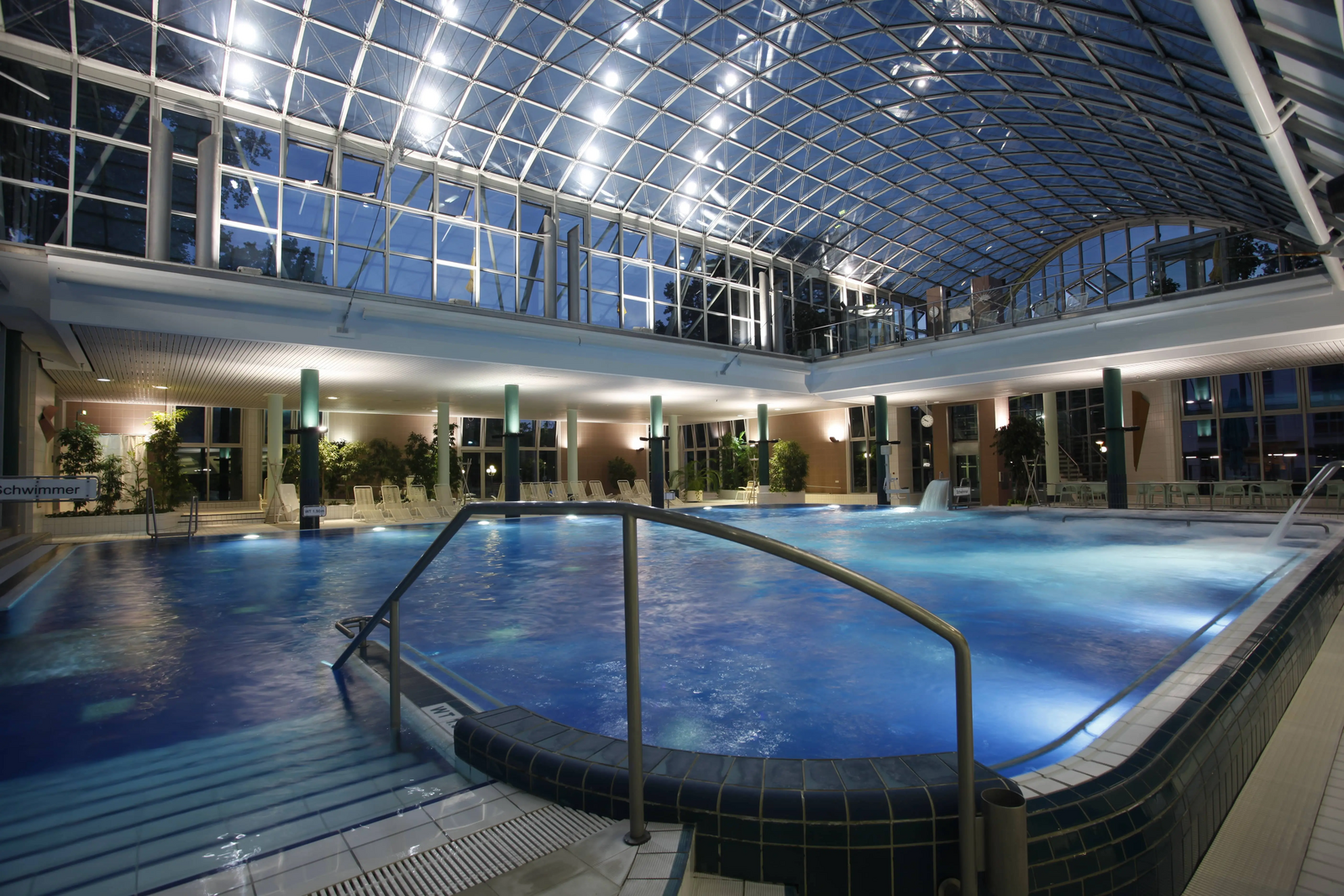 Nachtaufnahme. Beleutetes Bad. Blick auf das Innenschwimmbecken und die einizigartige Architektur des Dachs.
