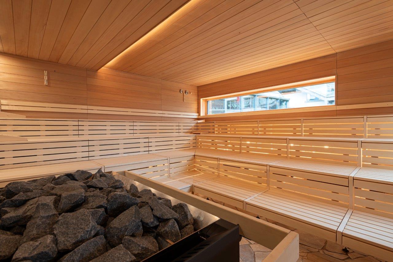Innenansicht Aussensauna im LEUZE. Baenke aus hellem Holz, Saunaofen, lichtdurchflutet.
