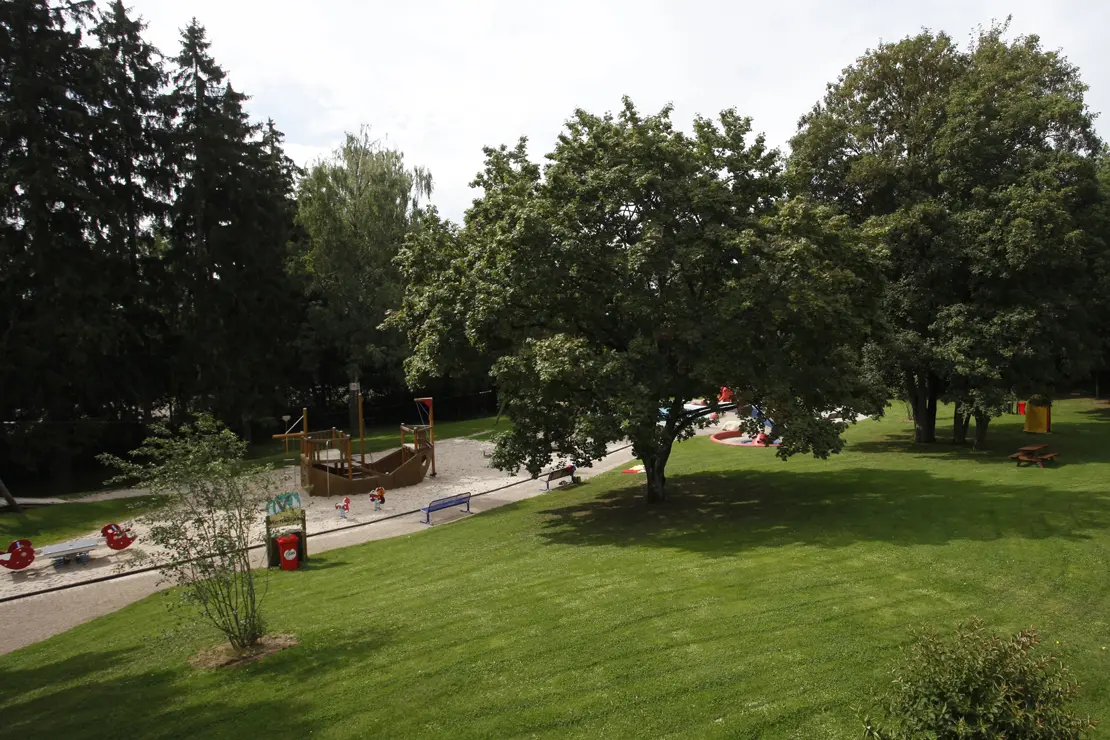 Spielplatz und Liegewiese Freibad Möhringen Außenansicht Spielplatz und Liegewiese mit Bäumen im Freibad Möhringen.