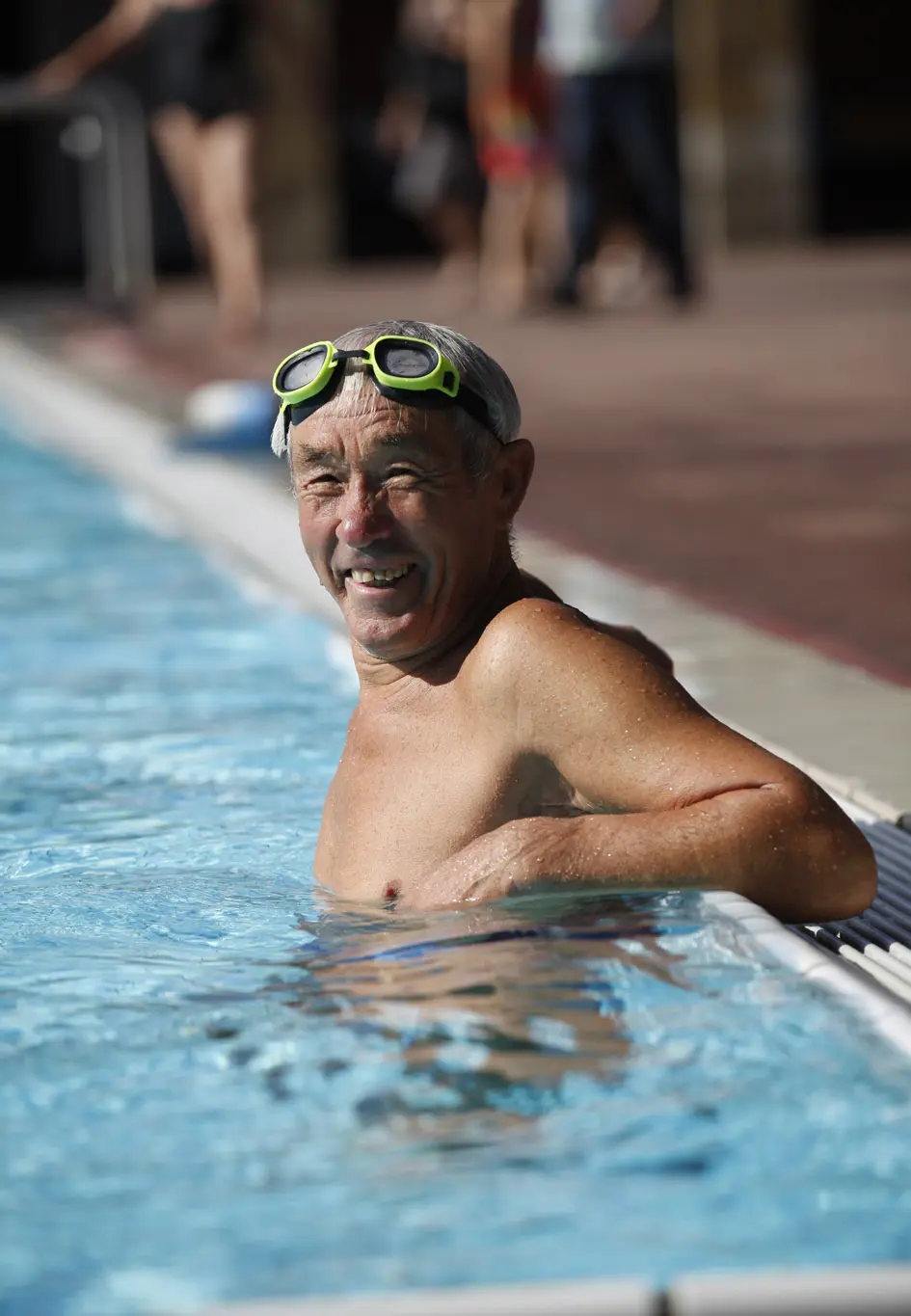 Ein fröhlicher Herr steht am Beckenrand im Schwimmbecken Höhenfreibad Killesberg.
